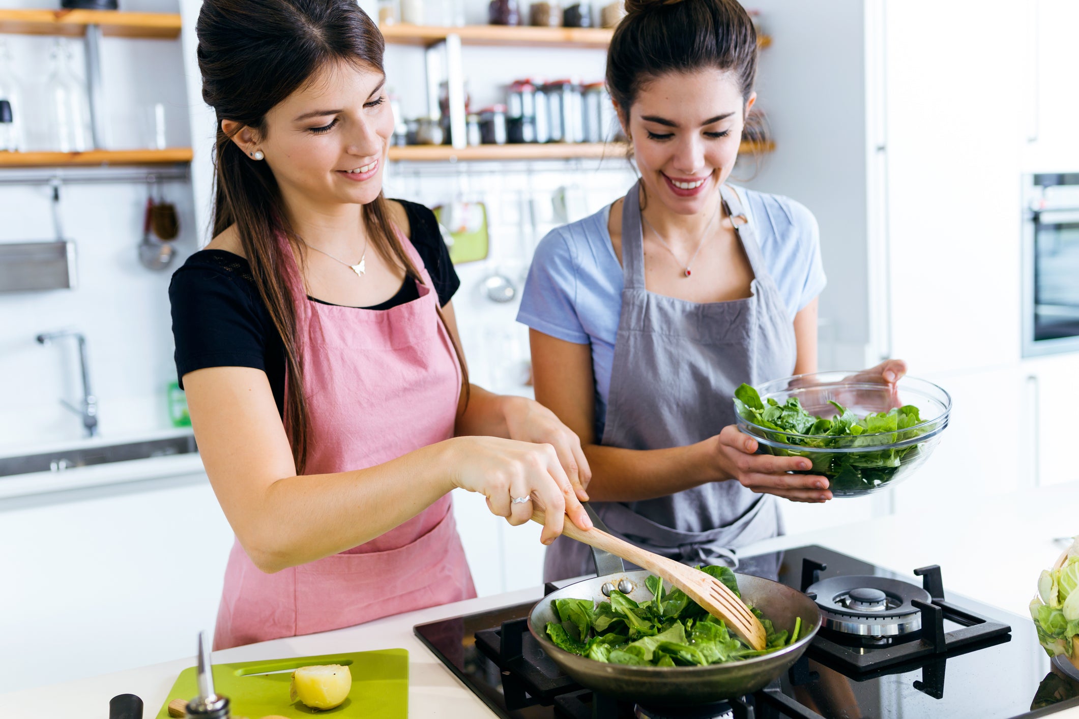 Two women cooking vegetables over a stone